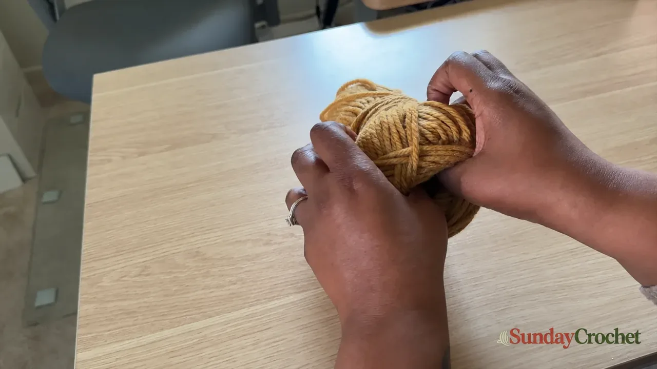 Hands finding the center-pull strand inside a mustard yarn skein