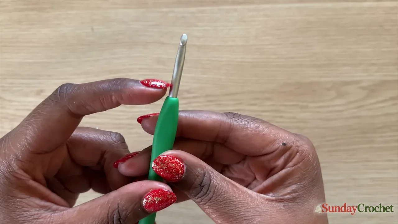 Close-up of hands holding a smooth aluminum crochet hook with an ergonomic green handle