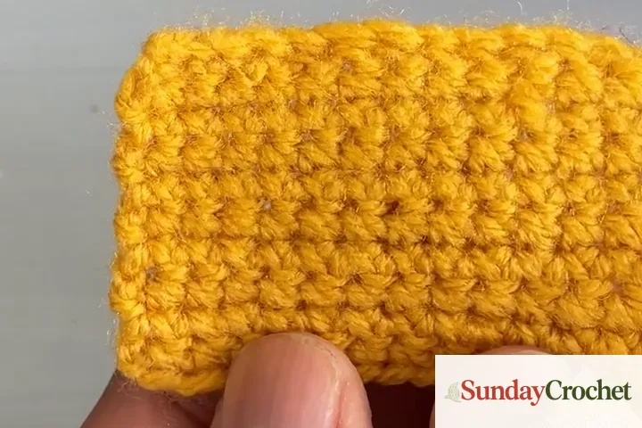 Golden acrylic single-crochet swatch held beneath a matching ball of yarn