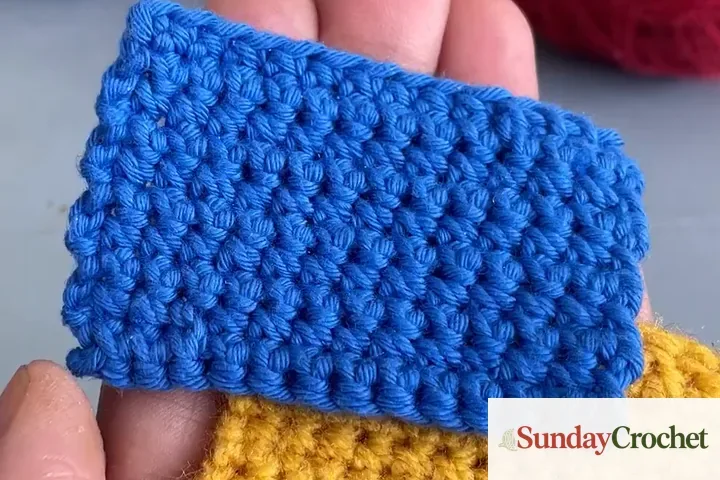 Blue cotton crochet swatch showing defined stitches held above a golden acrylic swatch