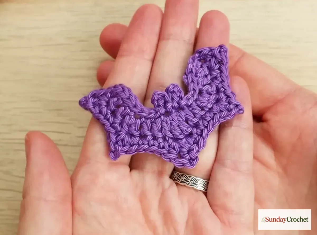 Finished purple crochet bat applique with pointed ears and shaped wings resting in a hand