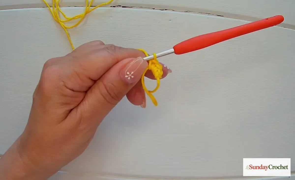 Hands crochet the yellow daisy center by working single crochet stitches into an adjustable magic ring