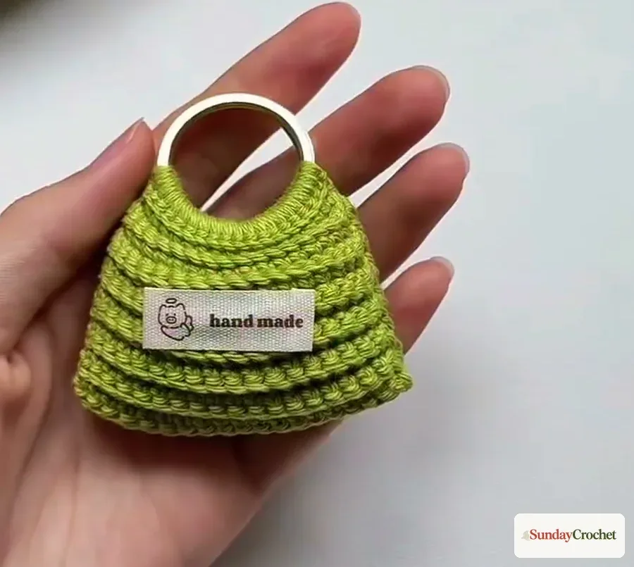 Finished lime-green mini crochet bag with a round gold ring handle resting in a hand