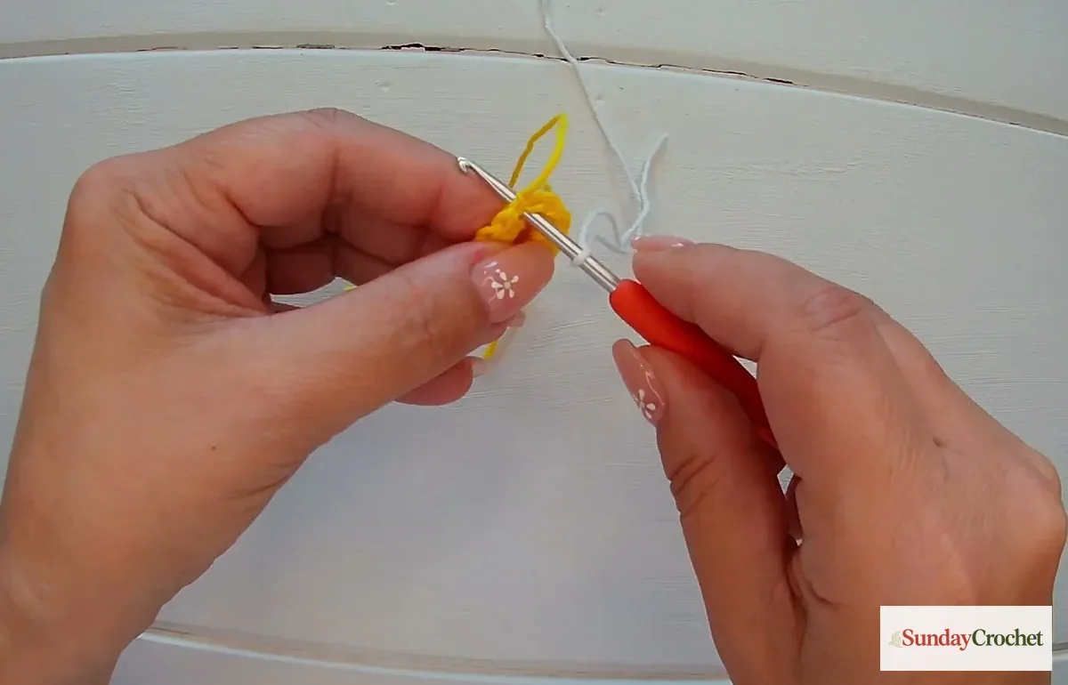 Hands join white yarn to the yellow crochet center before beginning the daisy petals