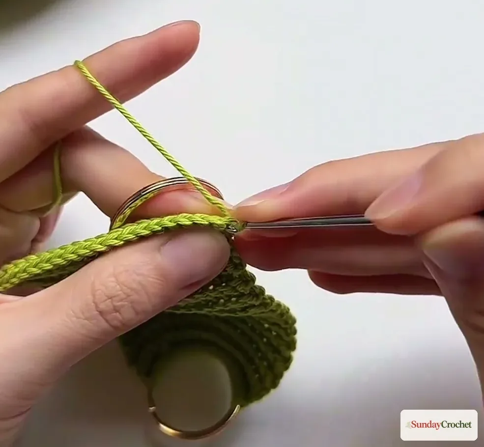 Green crochet stitches are worked around the second metal ring at the opposite end of the bag panel