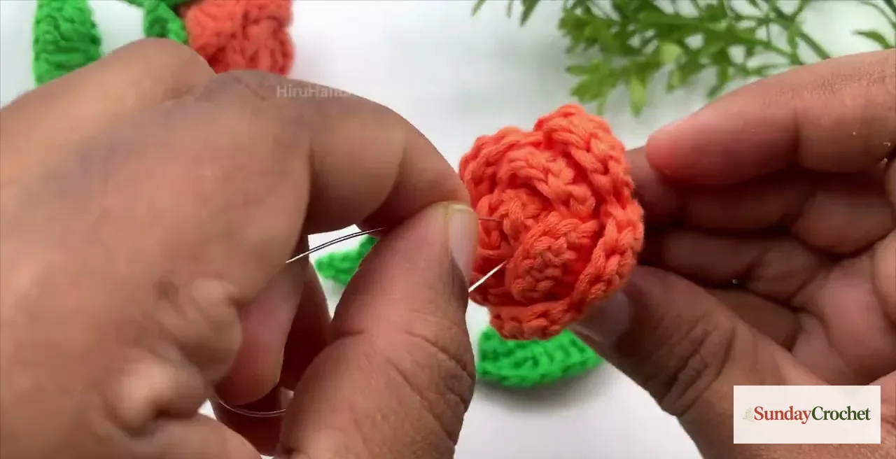 A yarn needle sews the coral rose to the green crocheted flower base