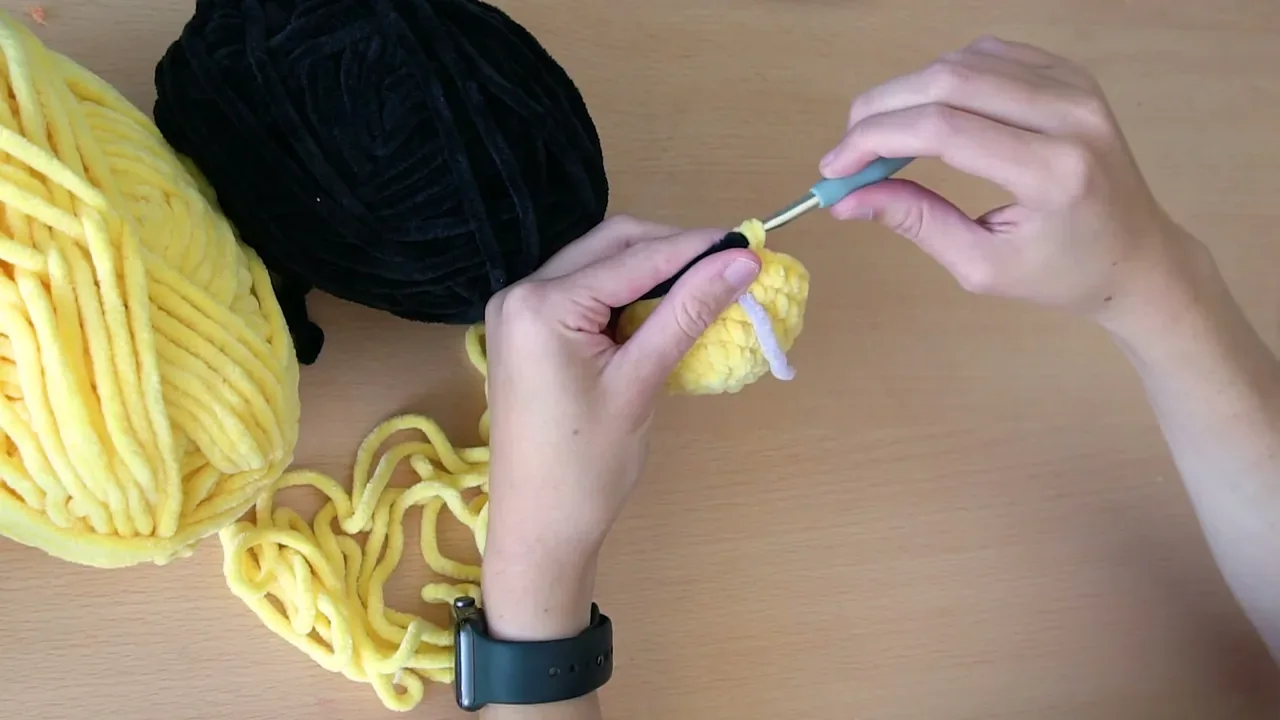 Hands change from yellow to black yarn at the final stitch before crocheting the bee's first black stripe