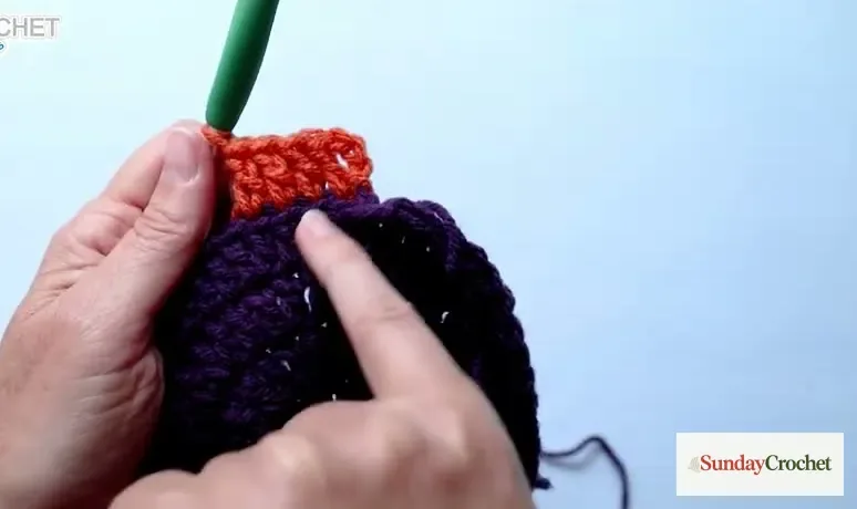Hands crochet orange background stitches around the purple cauldron circle