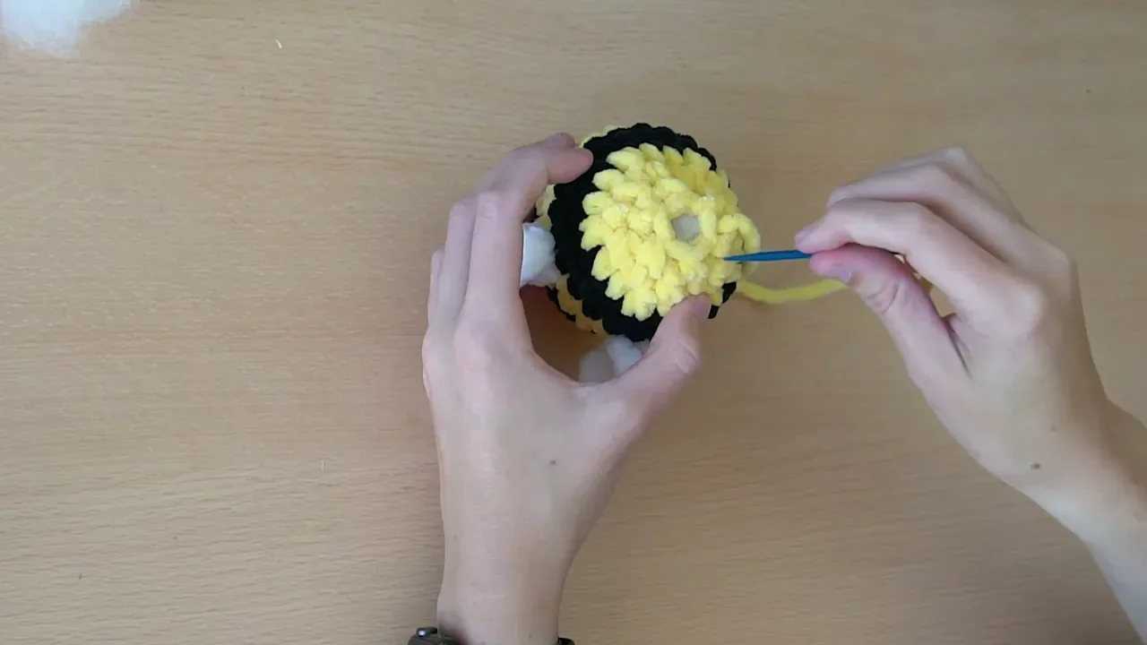 A yarn needle closes the small opening at the end of the stuffed crochet bee