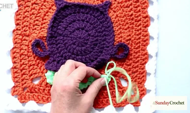 Hands sew a mint-green bubbling applique beneath the purple cauldron rim