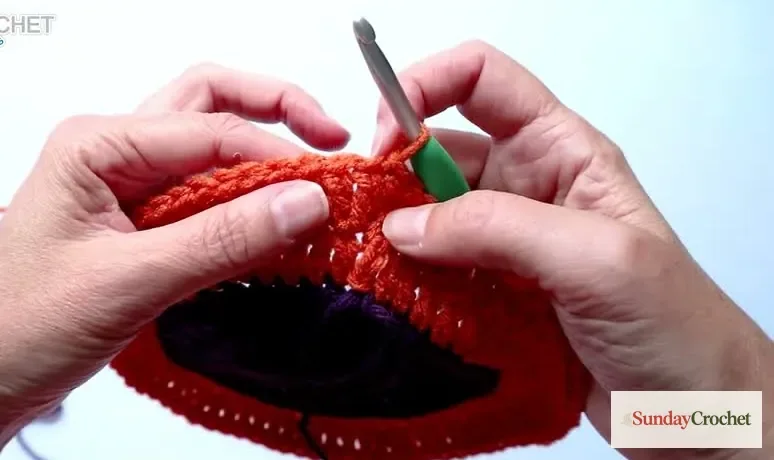 Hands work orange crochet stitches to shape the circular cauldron motif into a square