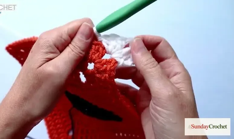 Hands crochet a white shell border along the orange granny square