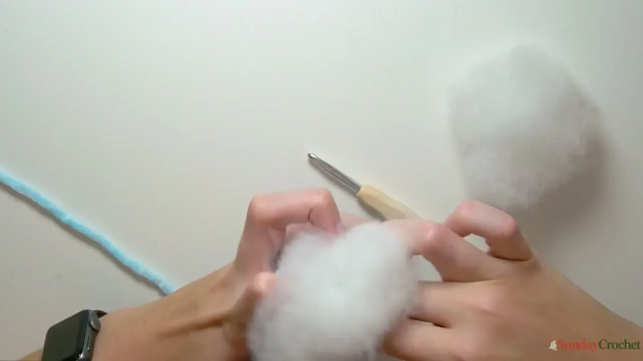 Hands add fiber stuffing to the crocheted dolphin body before closing the rounded snout