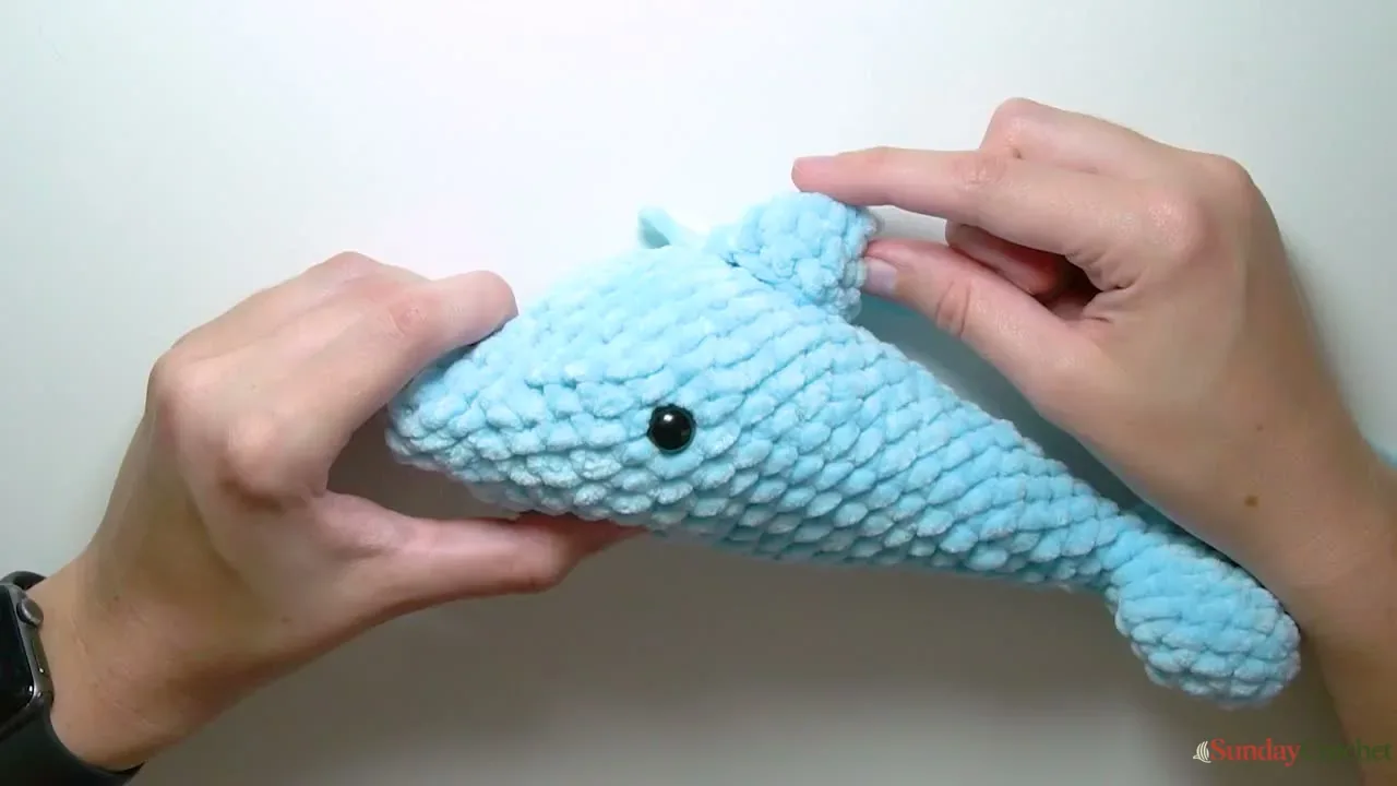 A crocheted dorsal fin is positioned on top of the dolphin behind its safety eye