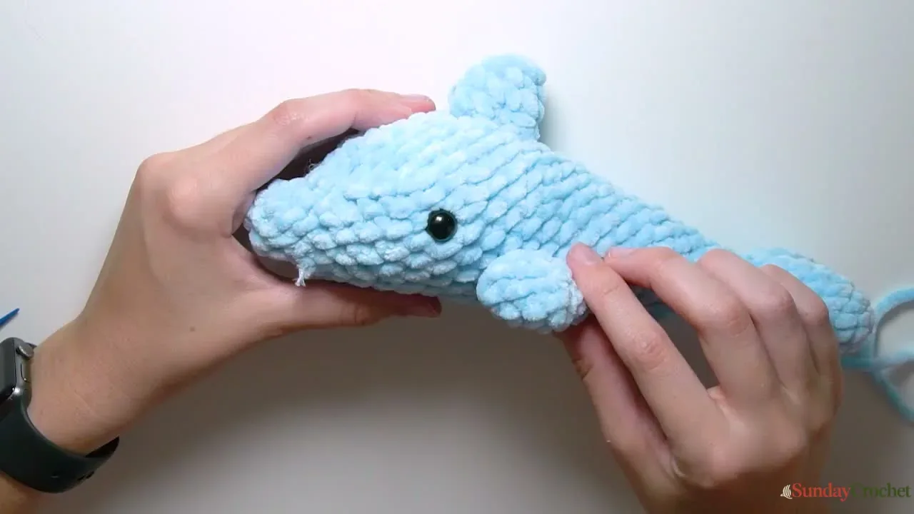 Hands sew a small side fin onto the blue crochet dolphin body