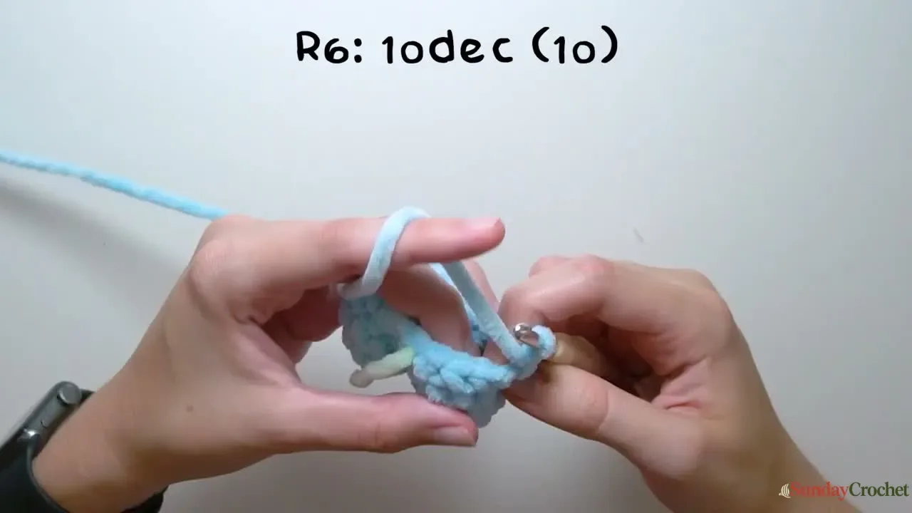 Hands crochet the small dolphin tail section in plush blue yarn before the body is shaped