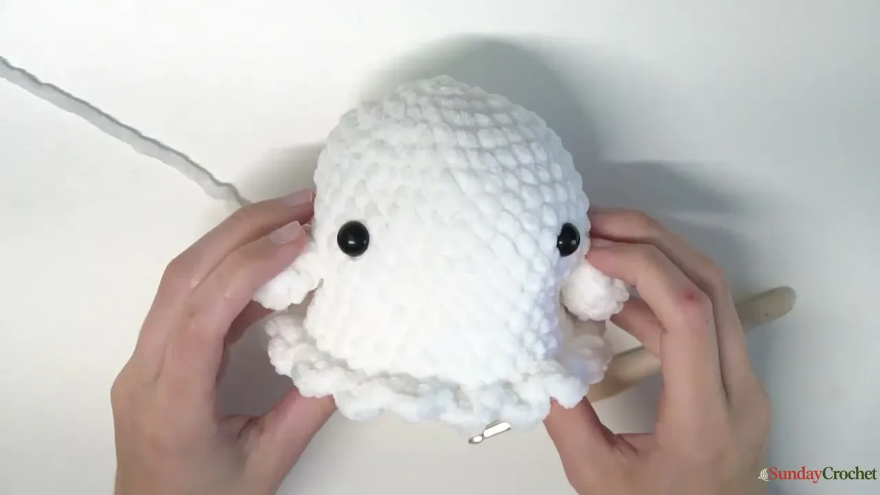 Black safety eyes are positioned on the white crochet ghost opposite the round marker