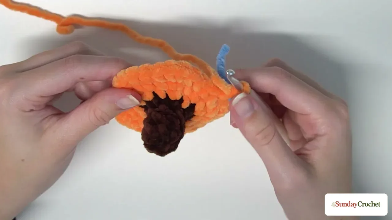 Hands work an orange increase round around the brown crocheted stem to start the pumpkin body
