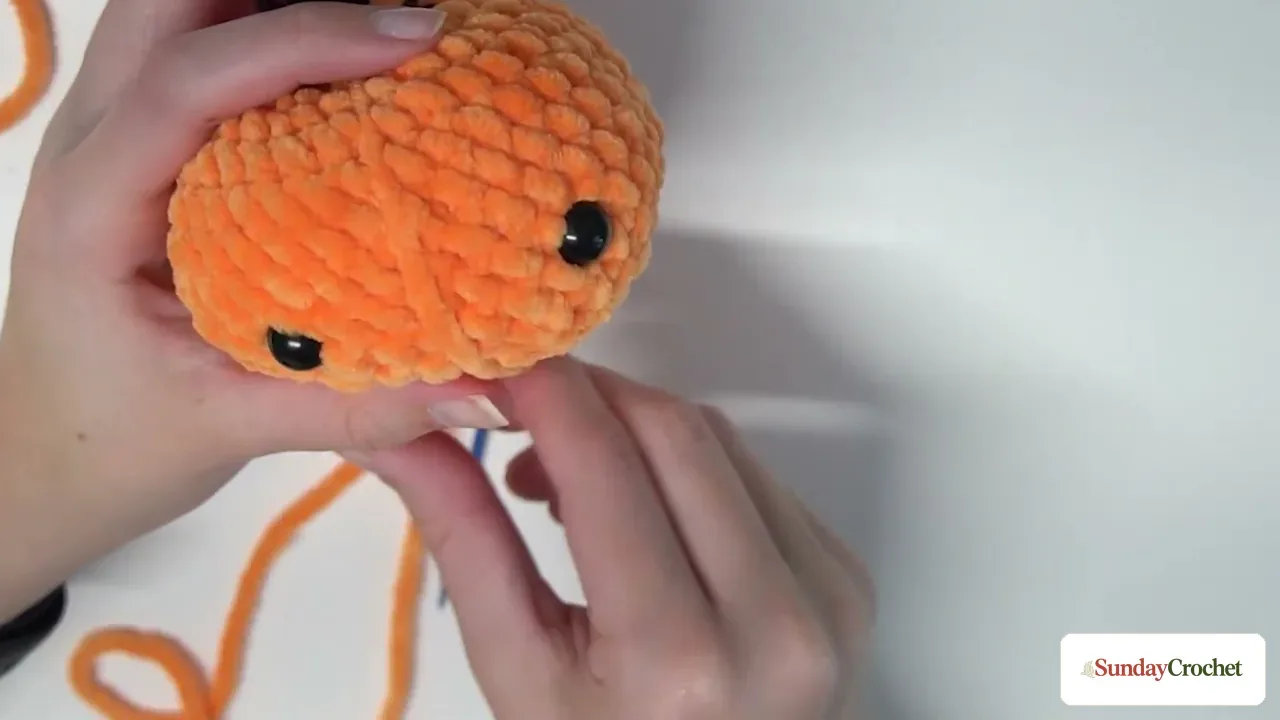 A yarn needle pulls the orange body inward to form one of the pumpkin's six ribs