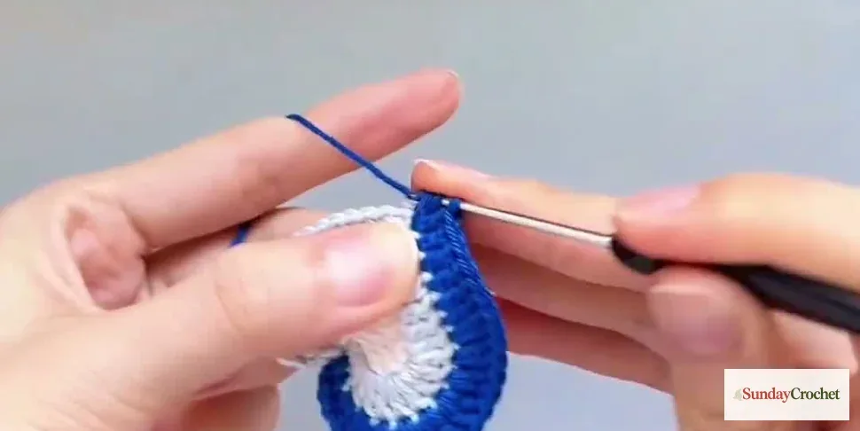 Hands work the bright blue edging around the white crochet heart