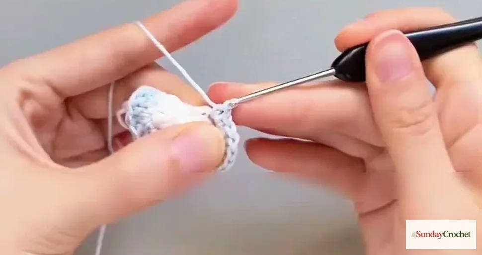 Hands shape the crochet heart with pale-blue stitches in the second round
