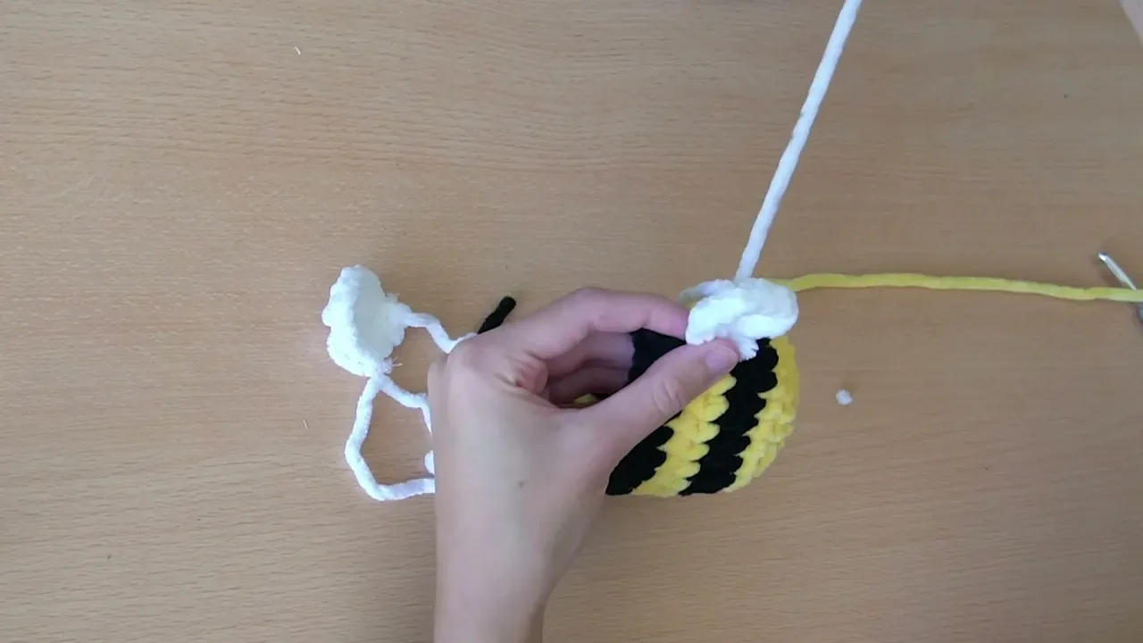 A white crochet wing is sewn securely to the top of the yellow and black bee body