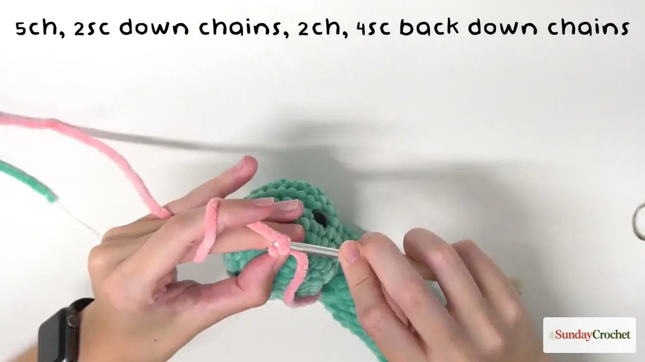 Hands crochet an optional pink forked tongue onto the center of the mint-green snake's snout