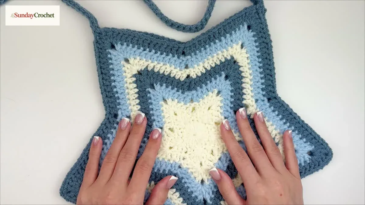 The finished star tote bag has a cream center, blue star points, and a matching crocheted strap