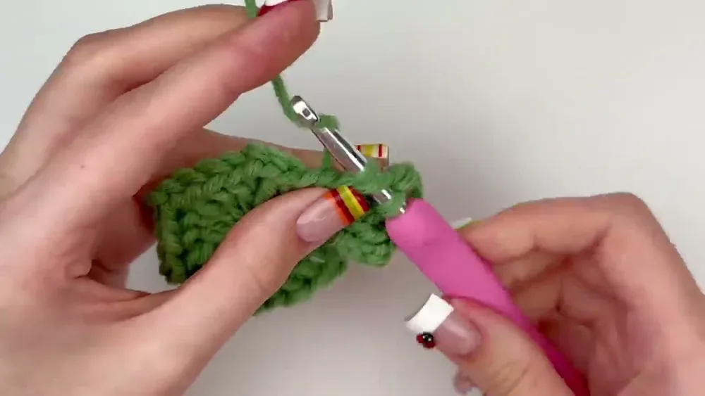 A hook works a three-double-crochet granny cluster into a chain-two corner space on the green hexagon
