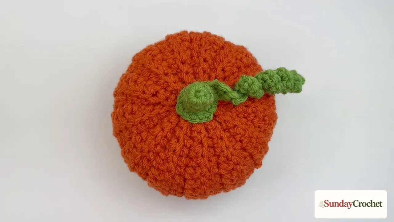 Finished rust-orange crochet pumpkin with raised ribs and an attached green stem and curly vine