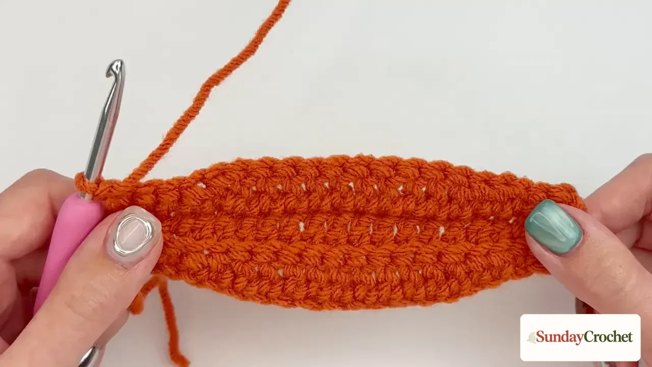 The completed orange ribbed crochet strip before its first and last rows are sewn together