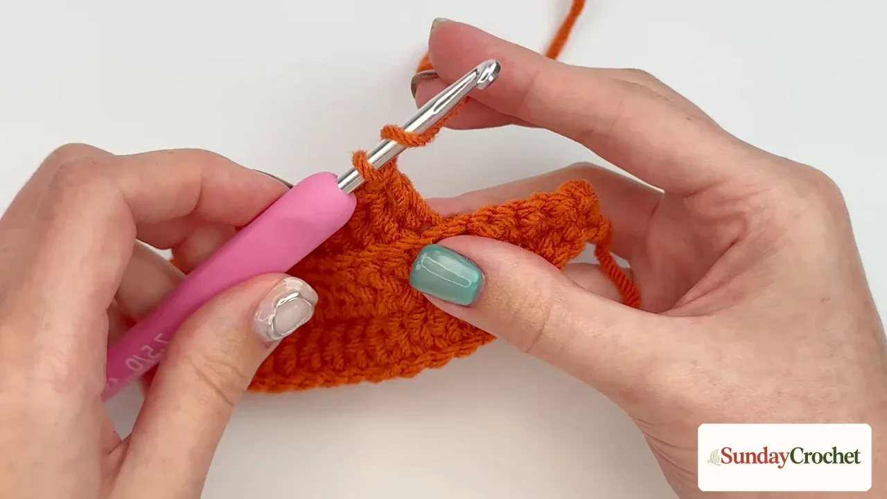 Hands crochet the orange pumpkin strip in repeated rows to create a ribbed texture