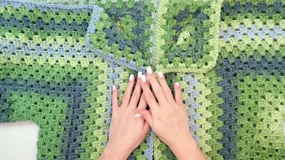 The green and blue crochet garment is positioned while its front seam is shaped to leave a neckline