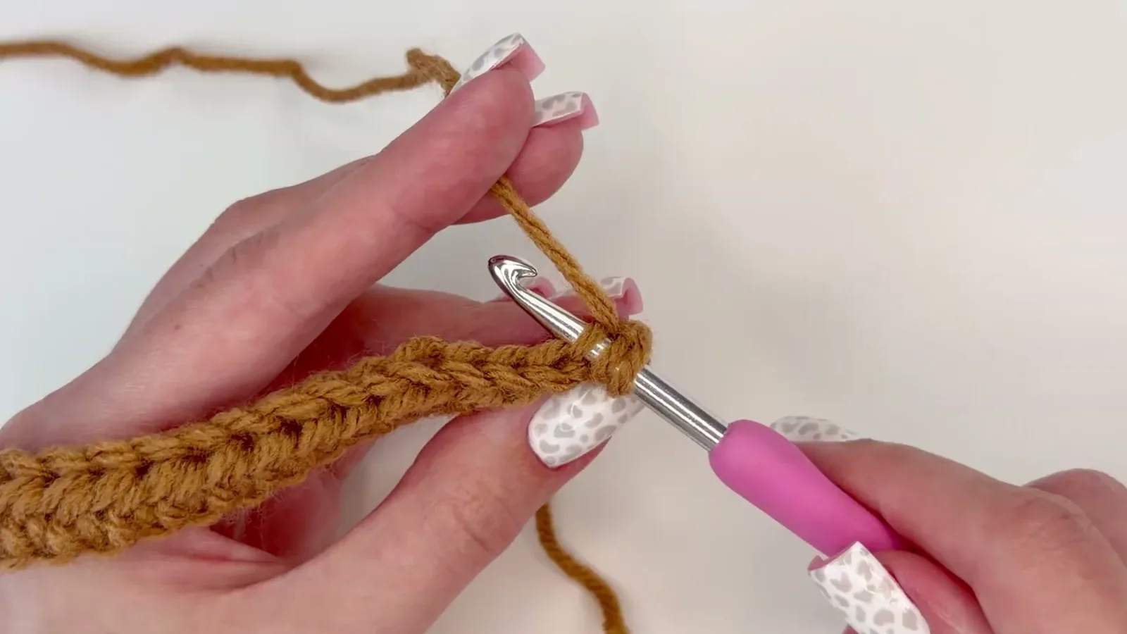 Crochet hook entering the back loop of a caramel half double crochet stitch