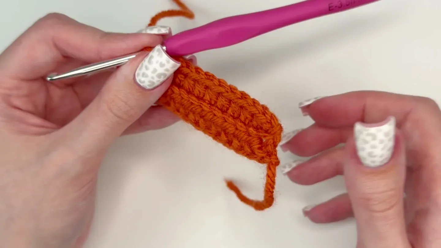 Hands work orange half-double crochet stitches into the back loops of a narrow pumpkin panel