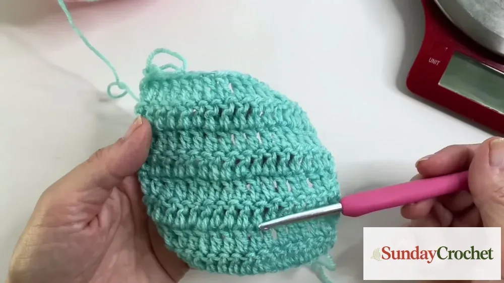 A turquoise crochet swatch held beside a hook to show the stitch texture used for an estimate.