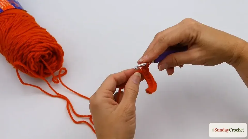 Hands making a double crochet stitch in orange yarn