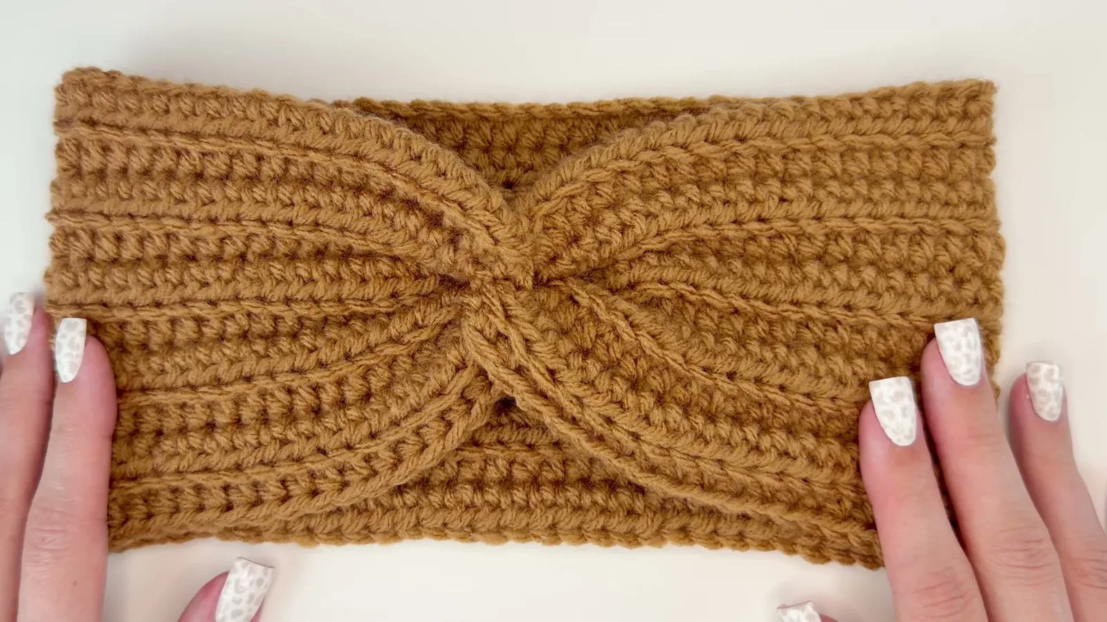 Finished caramel crochet ear warmer stretched flat to show its ribbing and central twist
