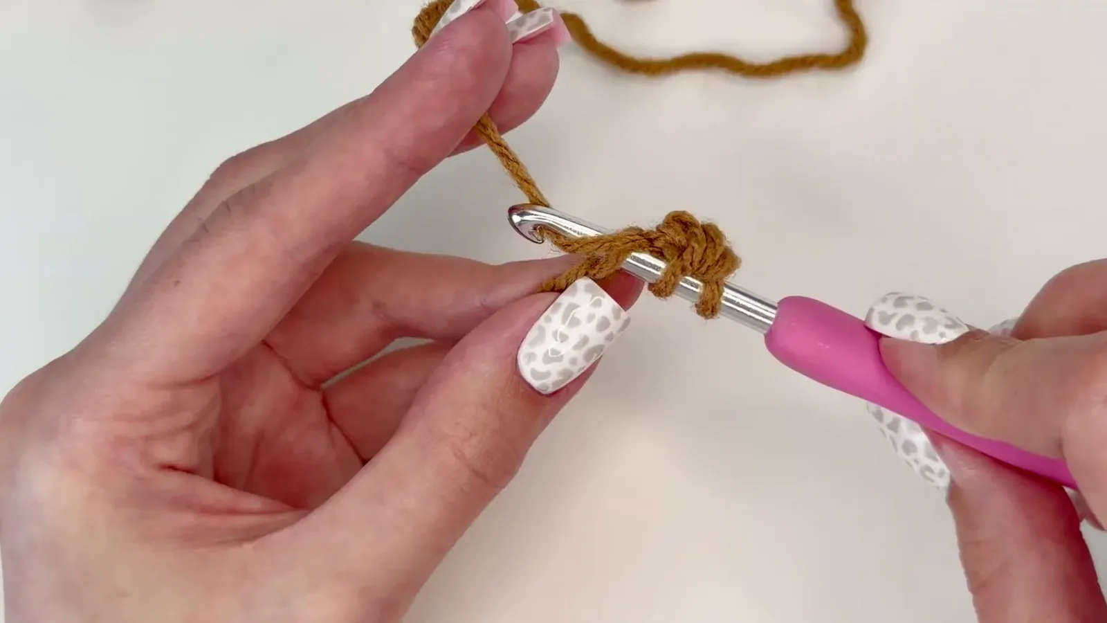 Half double crochet stitch worked into a foundation chain with a pink-handled hook and caramel yarn