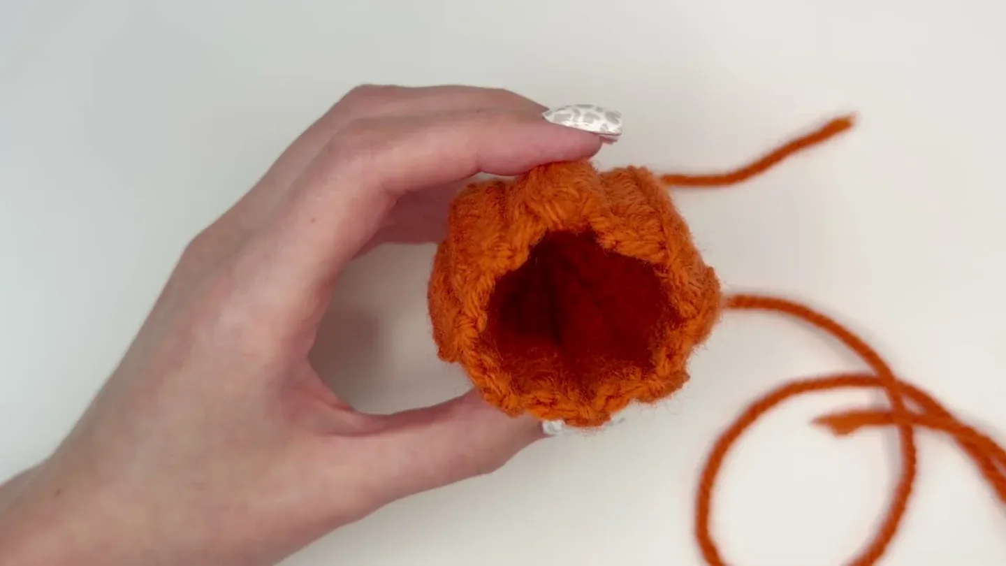 The orange crocheted tube is gathered at one end before stuffing is added inside