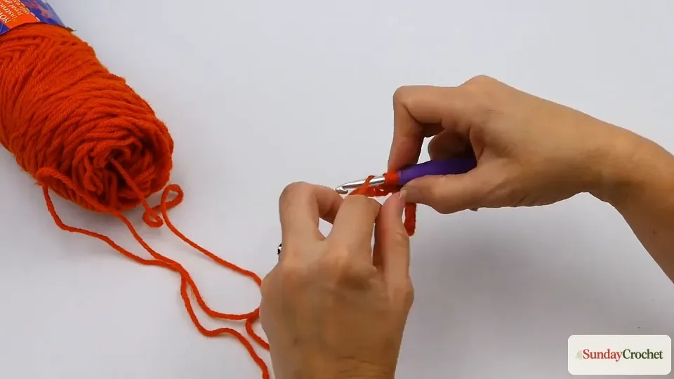 Hands making a half double crochet with three loops on the hook