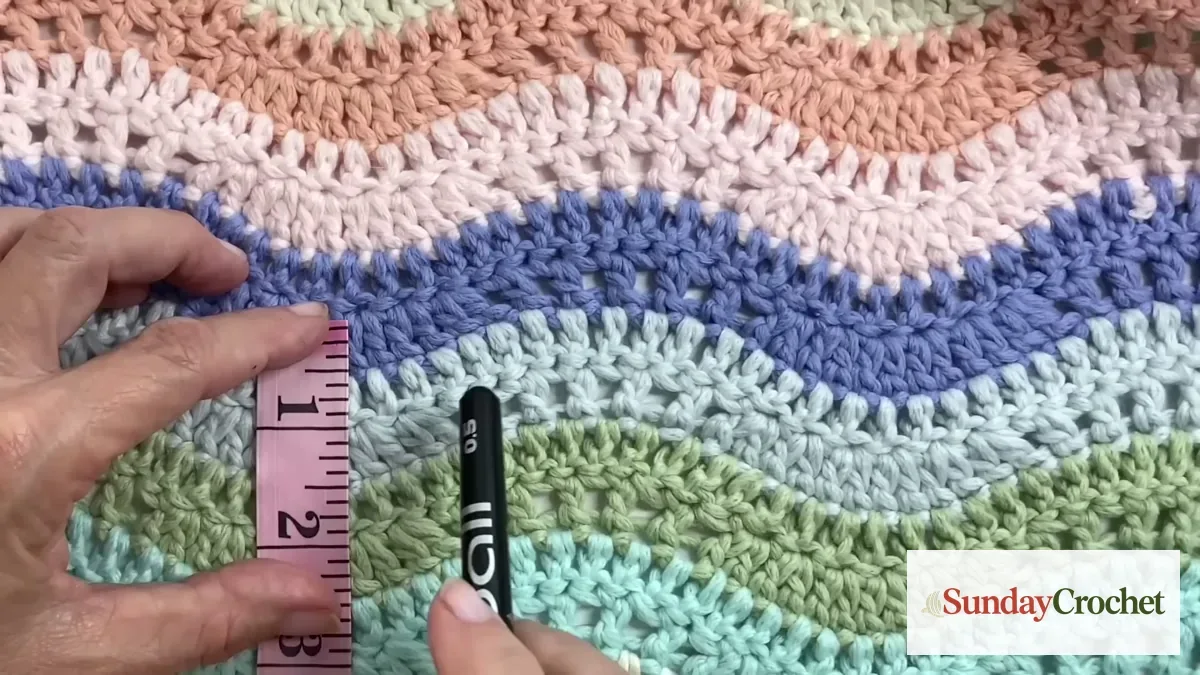 A measuring tape placed across the striped crochet blanket to check its width.