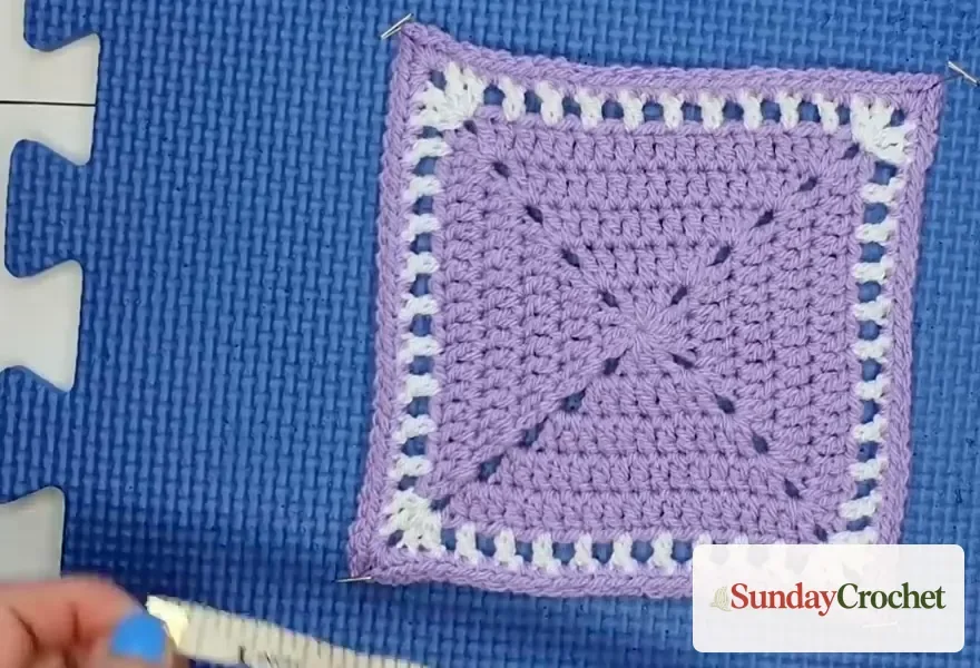 Tape measure checking the diagonal of a pinned lavender crochet square