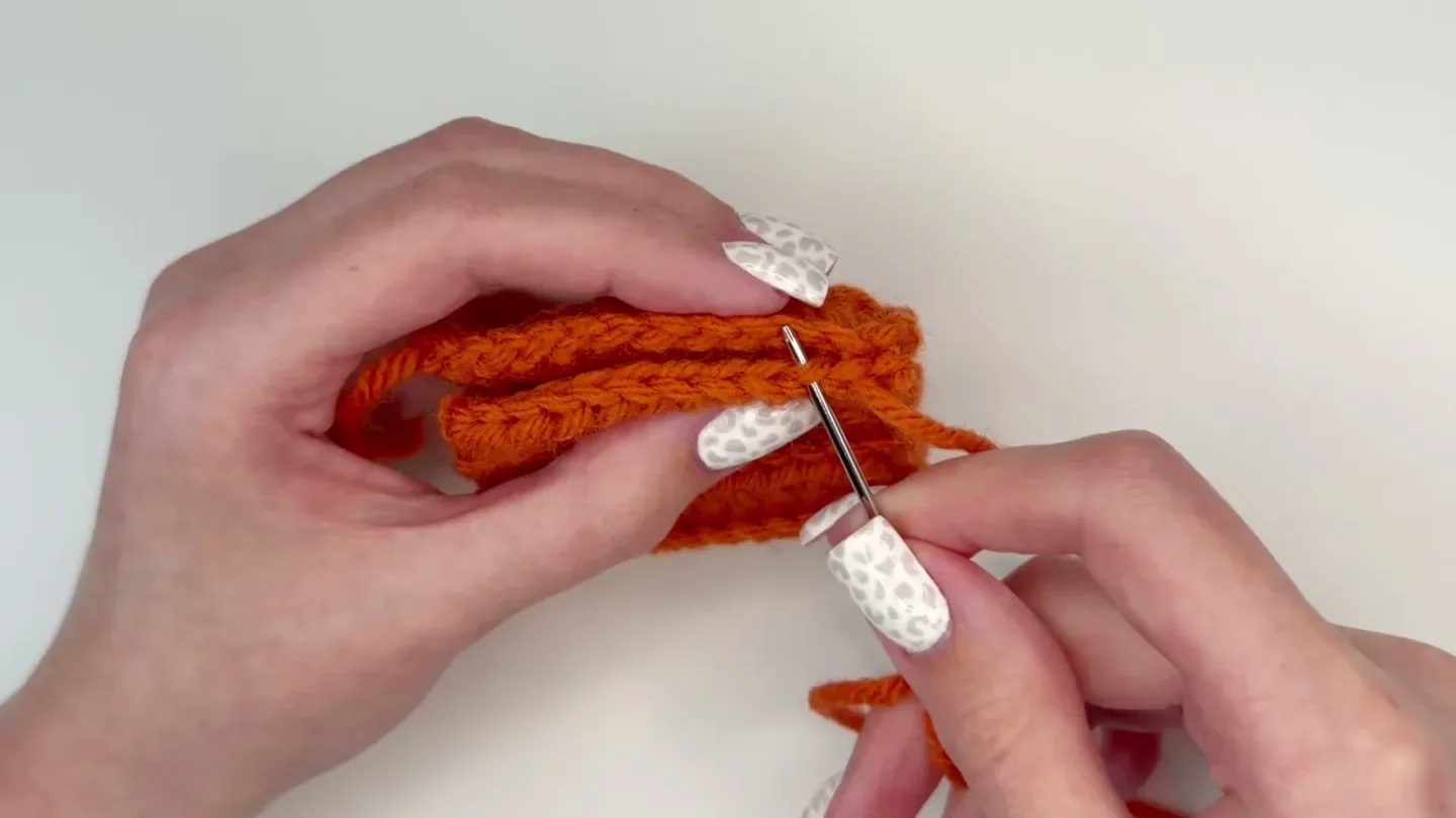 A tapestry needle sews the first and last row edges of the orange crochet strip together