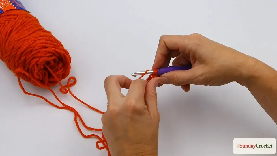 Hands working a single crochet stitch into an orange foundation chain