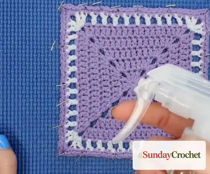 Hand misting a pinned lavender crochet square with a clear spray bottle