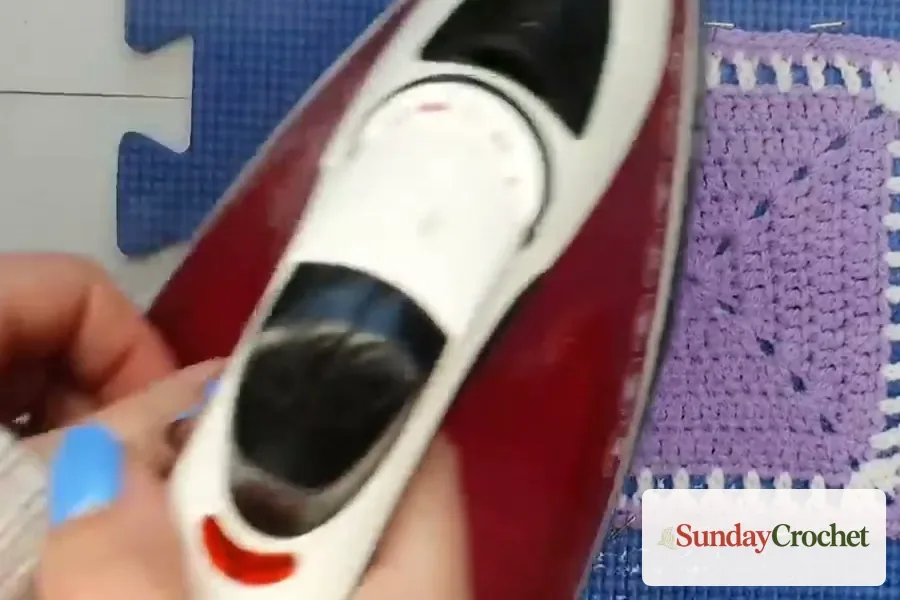 Steam iron held above a pinned crochet square without touching the fabric
