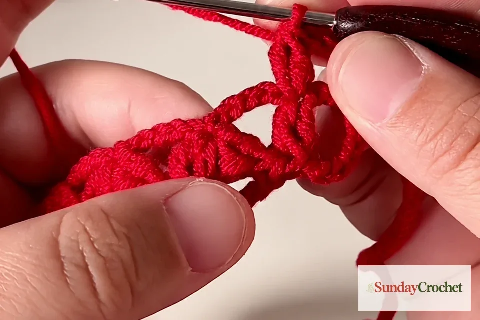 Red crochet lace with the hook positioned over a five-chain space between clusters