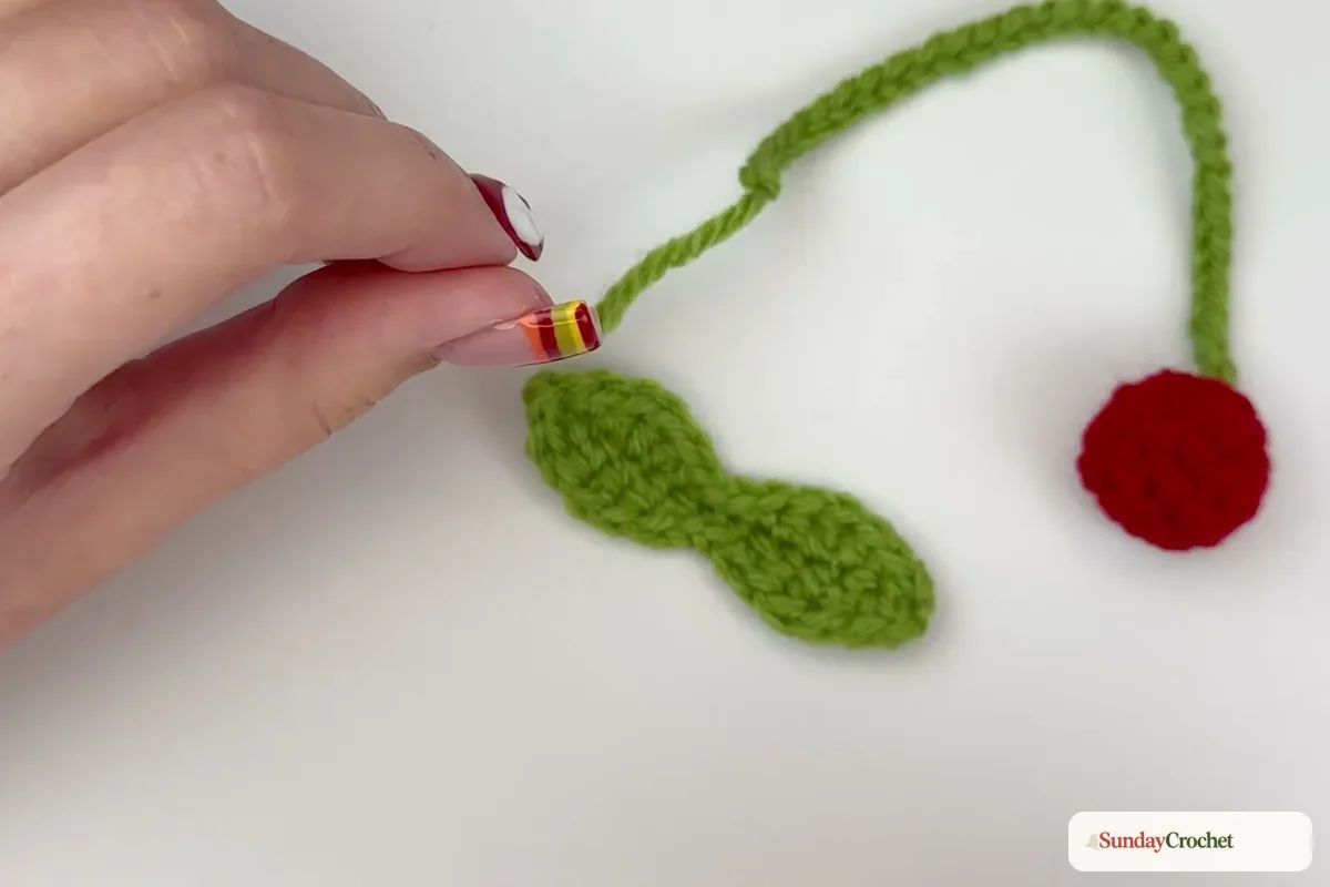 The two red cherries hang from a green chain and central crocheted leaf