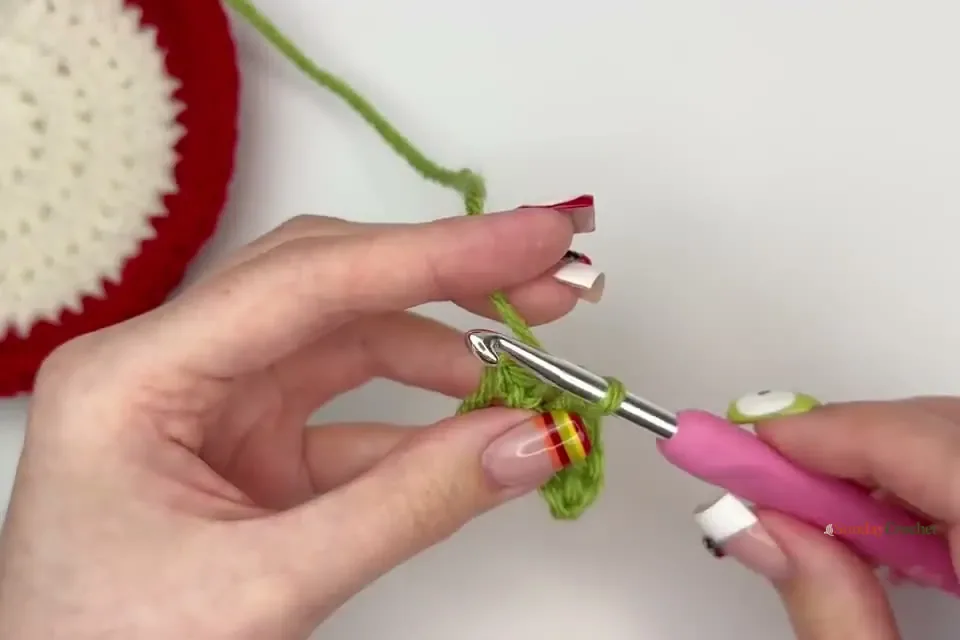 A small green crochet leaf is shaped by working stitches down both sides of a chain